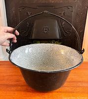 Full view of vintage black enamelware cooking pot with heavy metal handle and crackled interior.