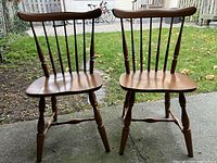 Front view of the two solid wood chairs showing contoured seats and spindled backs, placed outside on concrete.