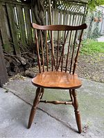 Front view of wooden Windsor style chair showcasing curved top rail, spindle back, and contoured seat on turned legs.