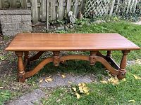 Solid wood coffee table outdoors on grass, showing front and detailed leg design with curved support beams.