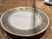Decorative plate with ornate blue and gold floral and scroll pattern around border and gold trim