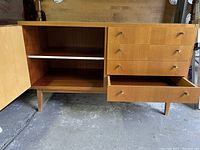 View of dresser with cabinet door open and one drawer open, showing interior shelf and wood finish inside the cabinet and drawers.