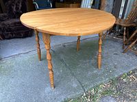 Side angle of the wooden kitchen table with one wing folded down showing turned legs and wood finish.