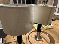 Pair of modern table lamps on wooden surface, one shade visibly bent