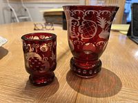 Photo showing front view of large and small ruby red glass vases with engraved decorative patterns on a wooden table