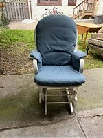 Front view of blue upholstered rocking chair with cushions, showing seat, armrests, and backrest.