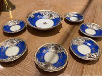 Top view of six blue, white and gold porcelain plates, including one large handled plate with a broken handle and five smaller matching plates