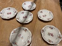 Seven porcelain plates with detailed floral designs and gold scroll accents on a wooden surface.
