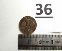 Photo showing medal next to ruler for size reference, approx 1.5 inches diameter.