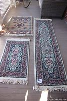 Photo showing three rug runners laid out on a porch floor — two matching floral patterned runners and one geometric patterned rug.
