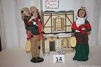 Full shot of the lot showing three Byers' Choice Christmas figurines: Bob Cratchit holding Tiny Tim and Mrs. Cratchit with holiday backdrop.