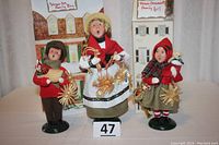 Front view of all three figures together: adult, boy, and girl holding straw ornaments and holiday items.