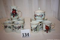 Photo showing 8 Lenox coffee mugs with Winter Greetings patterns, some with cardinal design and some with holly and ribbons.