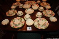 Full set of dinnerware and serving pieces laid out on wooden table showing floral desert rose pattern on all pieces