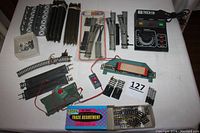 Wide view of all included HO scale model train components on white surface, showing transformer, tracks, switches, bridges, control buttons and dumping log car.