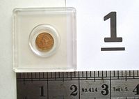 Coin in plastic capsule next to ruler showing ~15 mm diameter