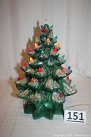 Front view of vintage green ceramic Christmas tree with multicolored lights and silver glitter on branches, star-shaped base visible, tagged 151