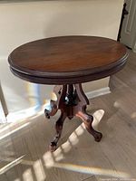 Angle showing the oval wood top and carved tripod legs of the antique table in natural light.
