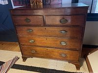 Front view of antique English Georgian Chippendale chest of drawers showing 5 oak drawers with brass escutcheons and original carved feet.