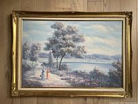 Full view of the large painting showing two Victorian ladies walking by a lakeside framed in an ornate gold painted frame.