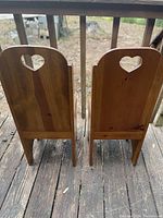 Back view of two pine child chairs showing heart-shaped cutouts on backrests and distinct wood grain.