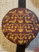 Top view showing full round lid with yellow hand painted birds, flowers, and berries on reddish-brown wood