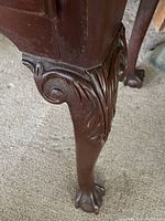 Close-up of a carved claw foot with scroll and leaf design on mahogany leg of the lowboy dresser.