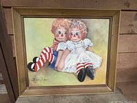 Full view of the painting showing Raggedy Ann and Andy seated against a light background, displaying the signature 'Doryce' and the gold tone mid-century frame.