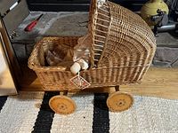 Side view of the natural wicker doll buggy with a fabric rag doll inside.