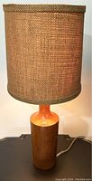 Full view of teak table lamp turned on with natural burlap shade showing texture and some visible wear.