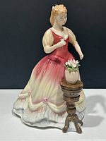 Front and side view of Royal Doulton Sarah figurine showing her pink and cream dress, sculpted roses, and pedestal with flower vase.