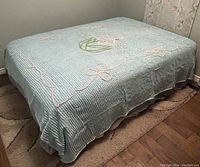 Light blue vintage chenille bedspread coverlet displayed on a bed, showing textured vertical stripes and embroidered floral patterns in pink and green.