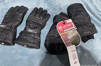Both pairs of gloves laid side by side showing the women's mitts with tags and men's leather gloves.
