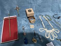 Wide shot of entire jewelry lot on blue cloth surface including crosses, pendants, necklaces, bracelets, watches, and earrings.