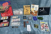 Overview of the lot showing stamps, currency, manuals, badges, playing card sets, toy tanks, shaving kit and comic book