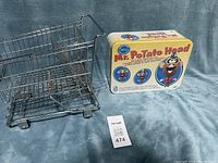 Photo shows vintage mini stainless steel shopping cart and sealed Mr. Potato Head tin side by side