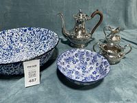 Lot showing entire tea set with enamel and ceramic bowls on blue backdrop
