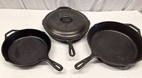 Three cast iron skillets arranged on a surface, one covered by a matching lid.