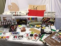 Wide view of entire art supply lot with paint tubes, palettes, brushes, canvases, pastels, mixing trays, and other materials on display