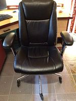 Front view of black leather office chair showing padded seat, backrest, and armrests with chrome base and caster wheels.