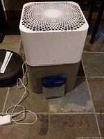 Photo of the Blueair air purifier unit showing white perforated top and gray fabric base, approximate size 13x20 inches.