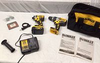 Overview of drill, impact driver, battery, charger, accessories and bag laid out on surface