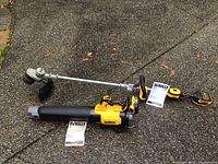 Full view on pavement showing string trimmer with shaft, blower with tube, two manuals laid out