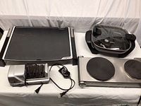 Overview photo showing all four items: the black Presto electric griddle, Oster electric skillet with glass lid, Deni two burner portable stove, and Chef's Choice knife sharpener.