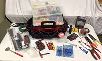Overview of the toolbox bag surrounded by multiple electrical tools and supplies, including testers, wire connectors, cable ties, tapes and pliers