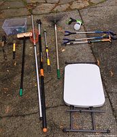 Photo showing the assortment of hand tools and fold-up table arranged on concrete surface outdoors.
