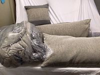 Two toned grey pillows and rolled comforter with textured fabric shown on white background.
