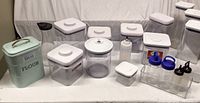 Full set of various kitchen storage canisters including the metal flour and bread tin, plastic canisters with white lids, and several plastic bottles and jars in a clear rack.