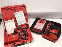 Hard plastic case open with compact driver drill, charger, two batteries, paperwork; soft carrying bag open with right angle drill, charger, paperwork