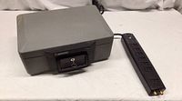 Closed grey Sentry Safe with key lock on front and RadioShack surge protector placed next to it.